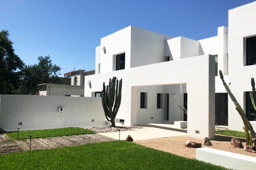 Hombre pintando la pared exterior de una casa con rodillo, mostrando un color claro.