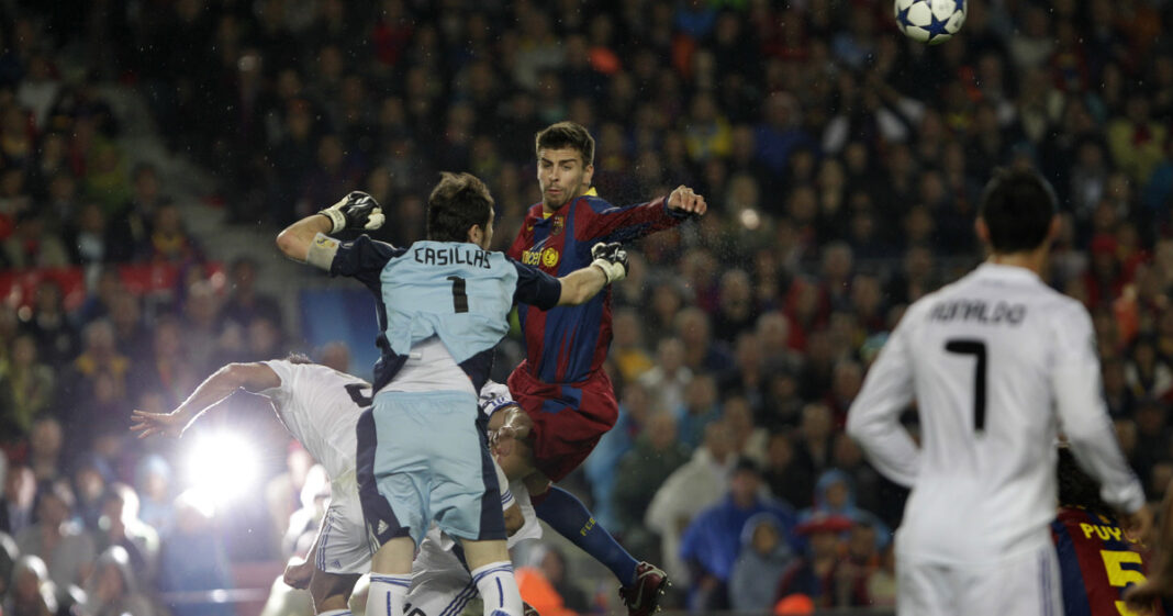 Gerard Piqué sonriendo en un evento, con fondo de un partido entre Barcelona y Real Madrid