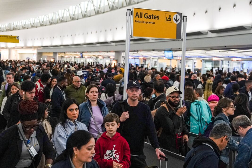 Pasajeros en fila de seguridad de aeropuerto con cartel de TSA
