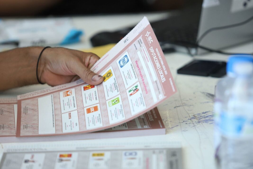 Personas votando en casilla electoral con urnas y credenciales