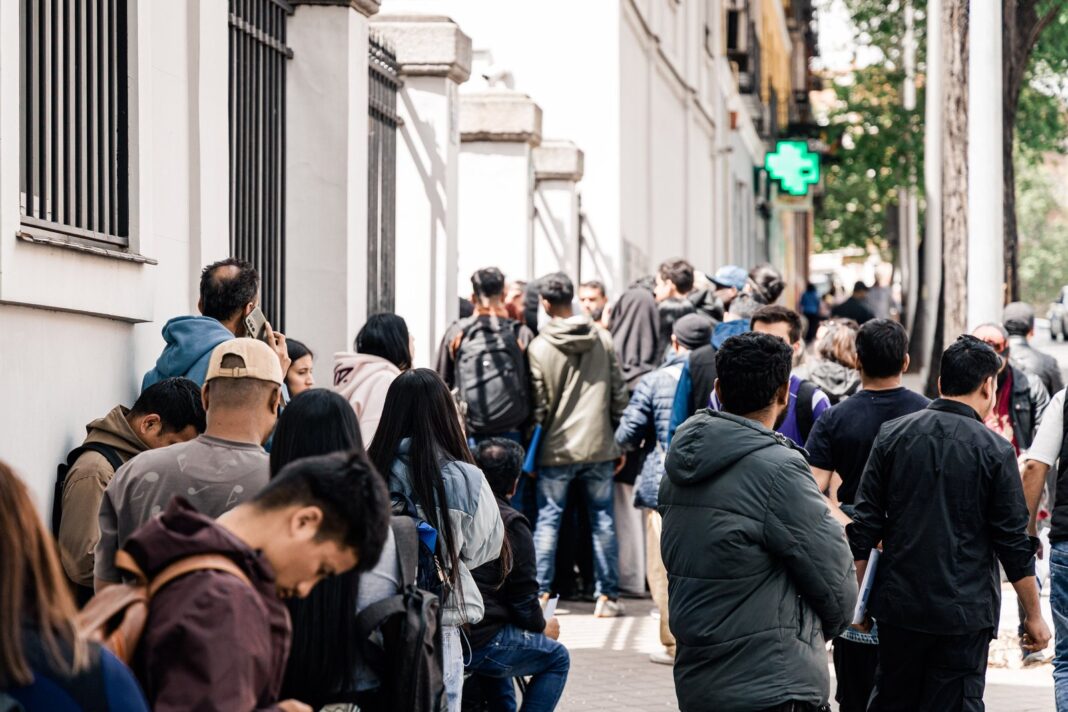 Personas migrantes en fila en una oficina de extranjería en España