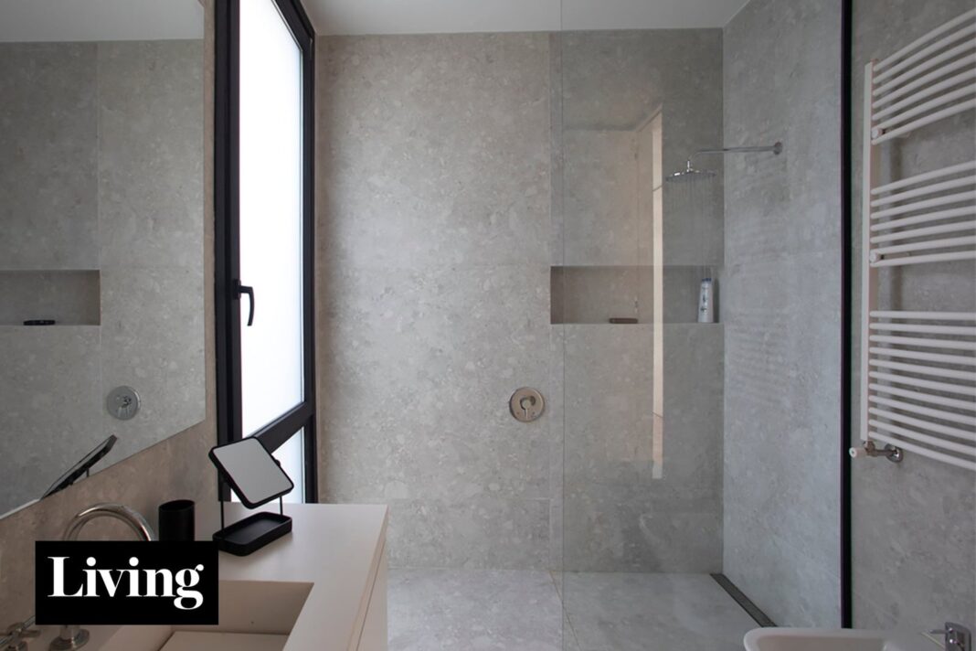Ducha al ras del piso con mampara de vidrio y revestimientos continuos en un baño moderno