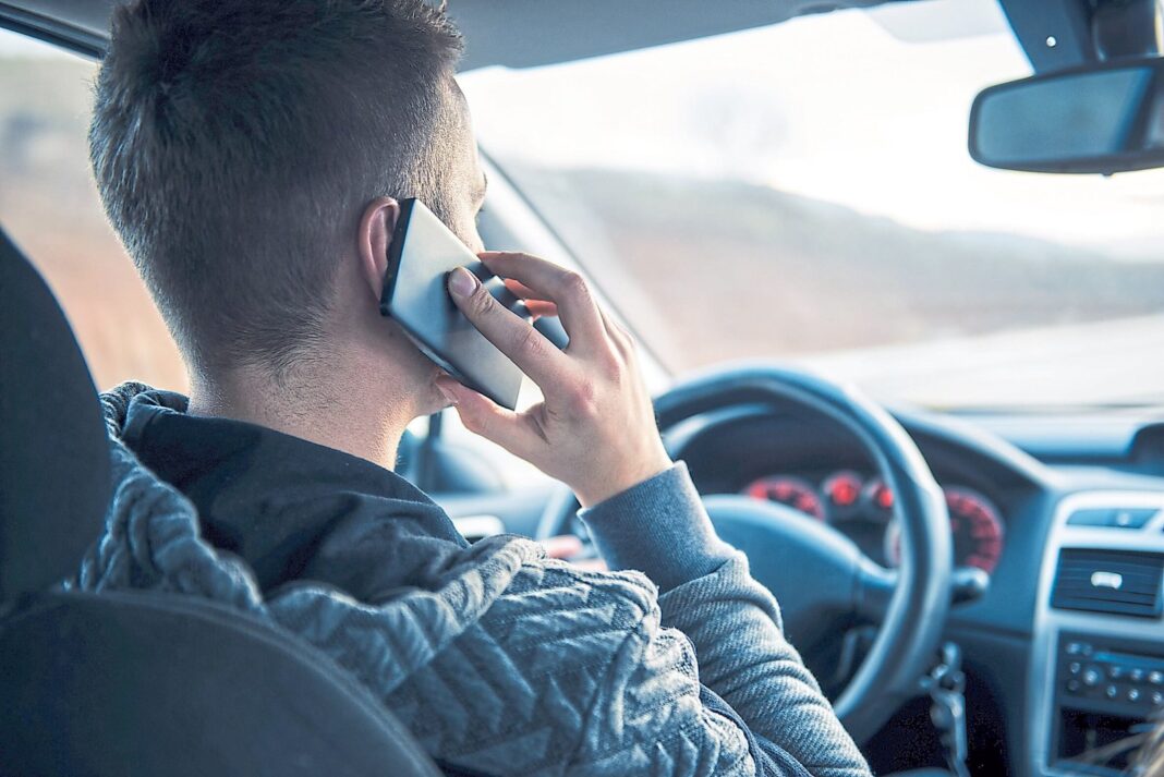 Conductor manipulando un teléfono celular mientras conduce un vehículo