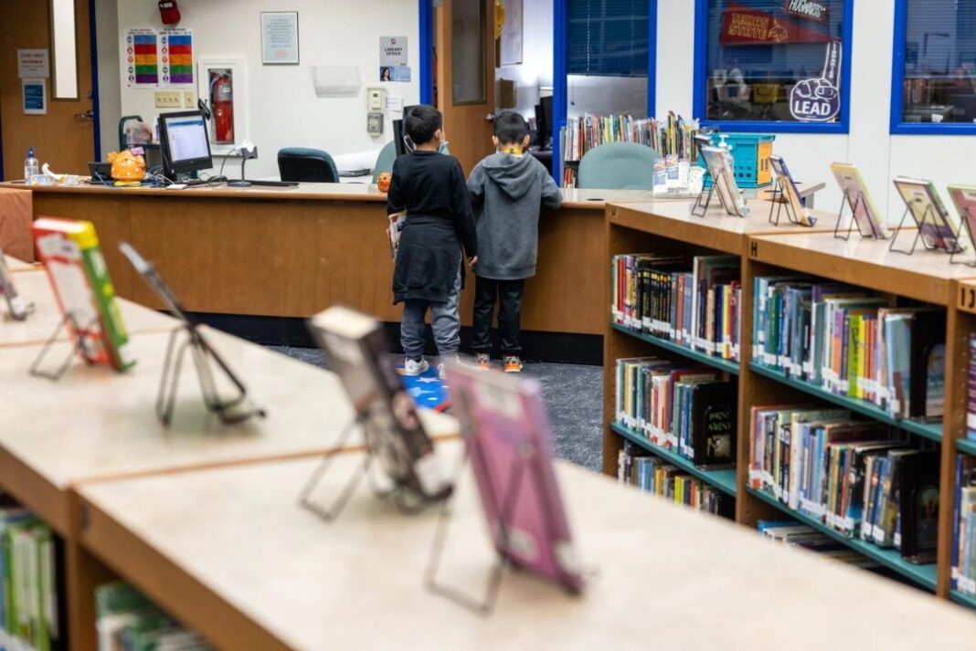 Estantería de biblioteca escolar con libros retirados y una lista de títulos vetados
