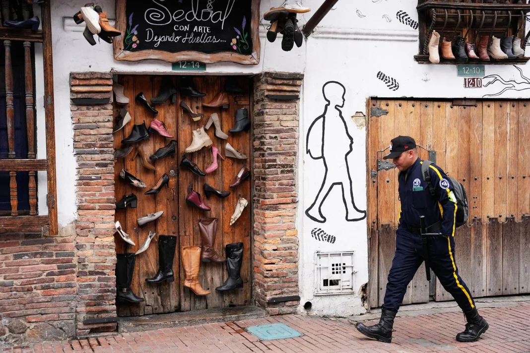 Guardia de seguridad caminando frente a un local con zapatos y botas colgando en su fachada en Bogotá